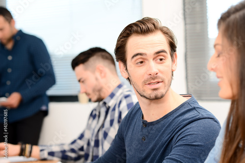 portrait of a candid handsome young man in high school classroom talking with woman friend classmate with teacher in background