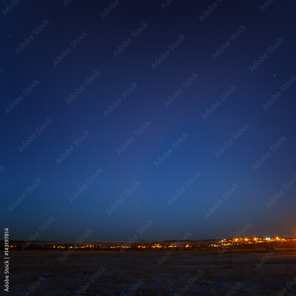 Starry sky above the urban outskirts with street lighting.