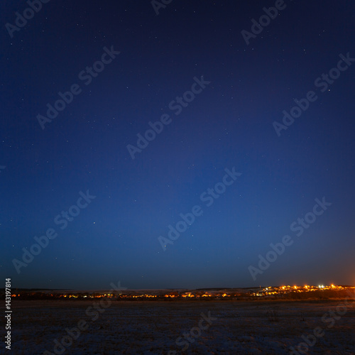 Starry sky above the urban outskirts with street lighting.