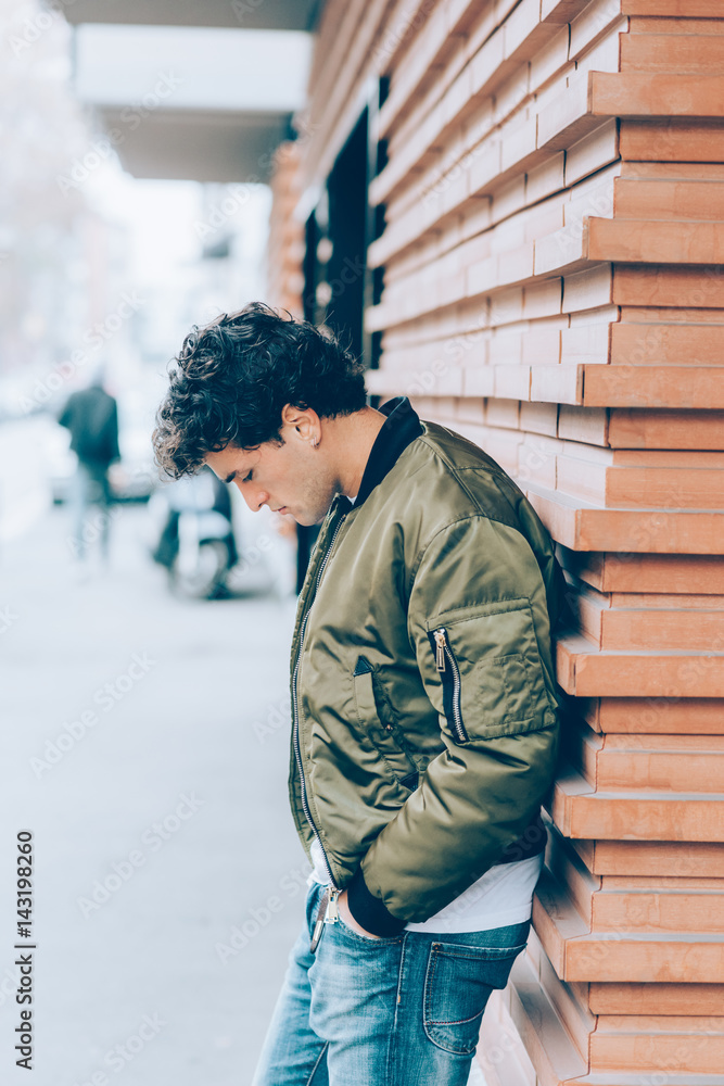 Handsome young man outdoor leaning wall looking away serious - customer, attitude, indipendent concept Handsome young man outdoor leaning wall looking away serious - customer, attitude, indipendent concept