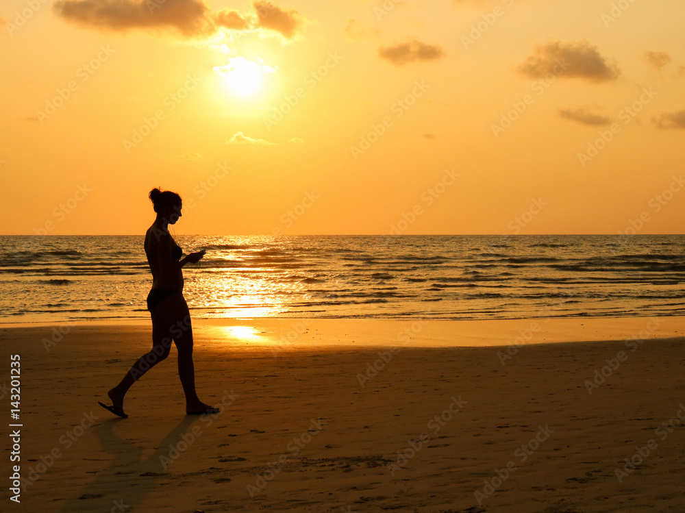 Women walking on the beach at sunset time. silhouette of the girl listen music on the beach.