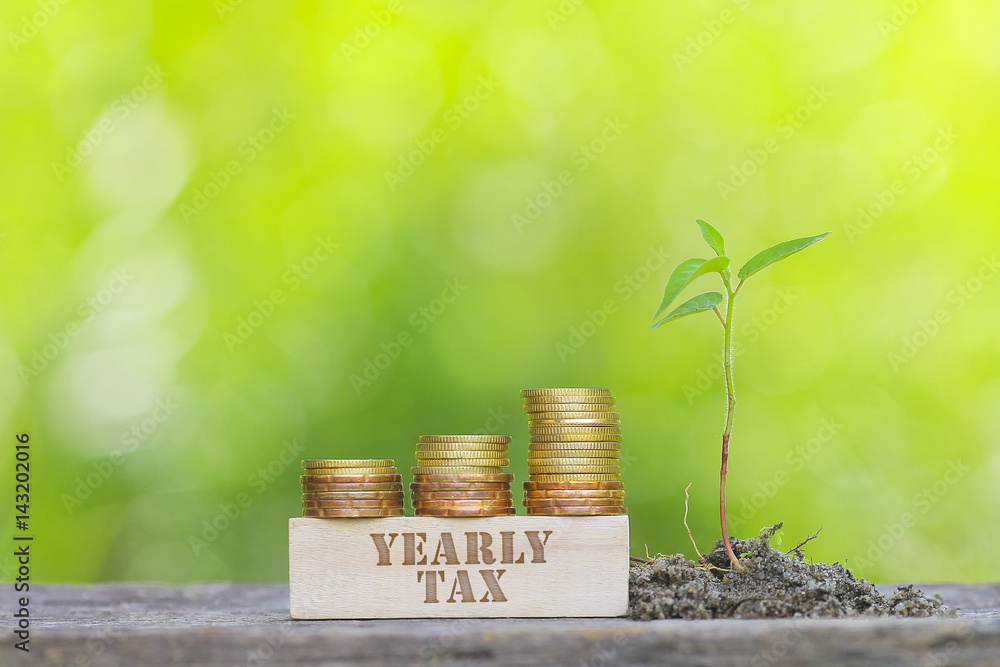 Φωτογραφία YEARLY TAX WORD Golden coin stacked with wooden bar on shallow DOF green background
