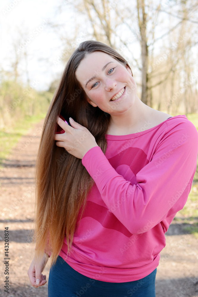 Fototapeta premium The portrait of beautiful young woman brushing her hair in the park.