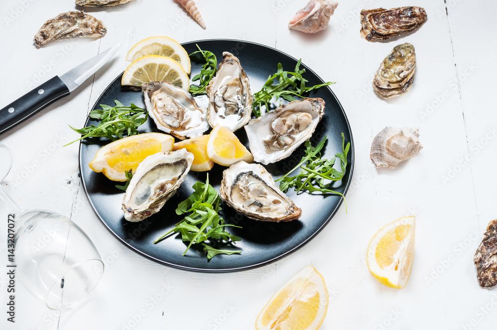 Oysters with lemon fruit on a black plate and glass of wine on a white wood table. Oysters with lemon fruit on a black plate and glass of wine on a white wood table.