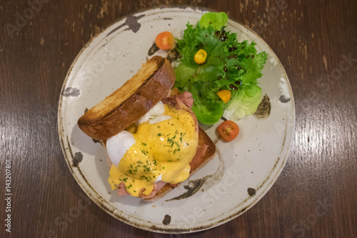 Eggs Benedict with Whole wheat toast, Poached eggs, Hoallandaise sauce, Ham and Fresh salad on a circle plate