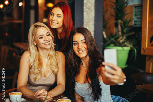 Three beautiful young woman doing selfie in cafe