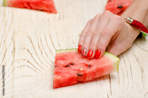 Triangular slice of watermelon in a female hand with red nails. Close-up