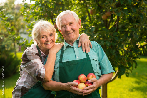 Senior couple with apples. Smiling people outdoors. Tips for gardening.