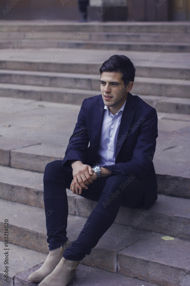 Handsome young man with styled hair. The man is sitting on the steps. 