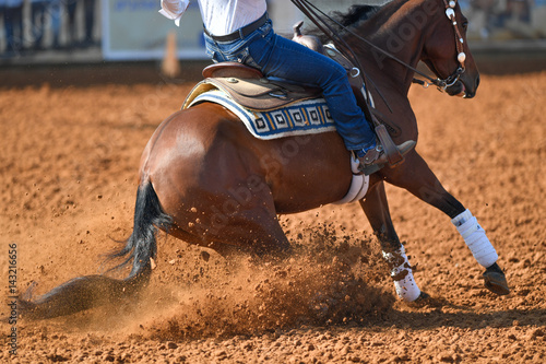 A side view of a rider sliding the horse in the dirt