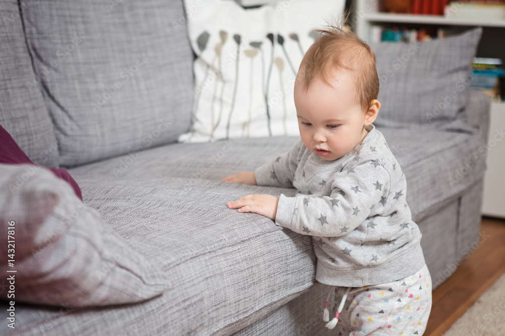 Eleven months old baby girl standing by the sofa Eleven months old baby girl standing by the sofa