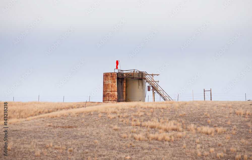 One newer and one old rusted oil tank with an attached ladder abandoned in a fenced pasture in spring Montana landscape One newer and one old rusted oil tank with an attached ladder abandoned in a fenced pasture in spring Montana landscape