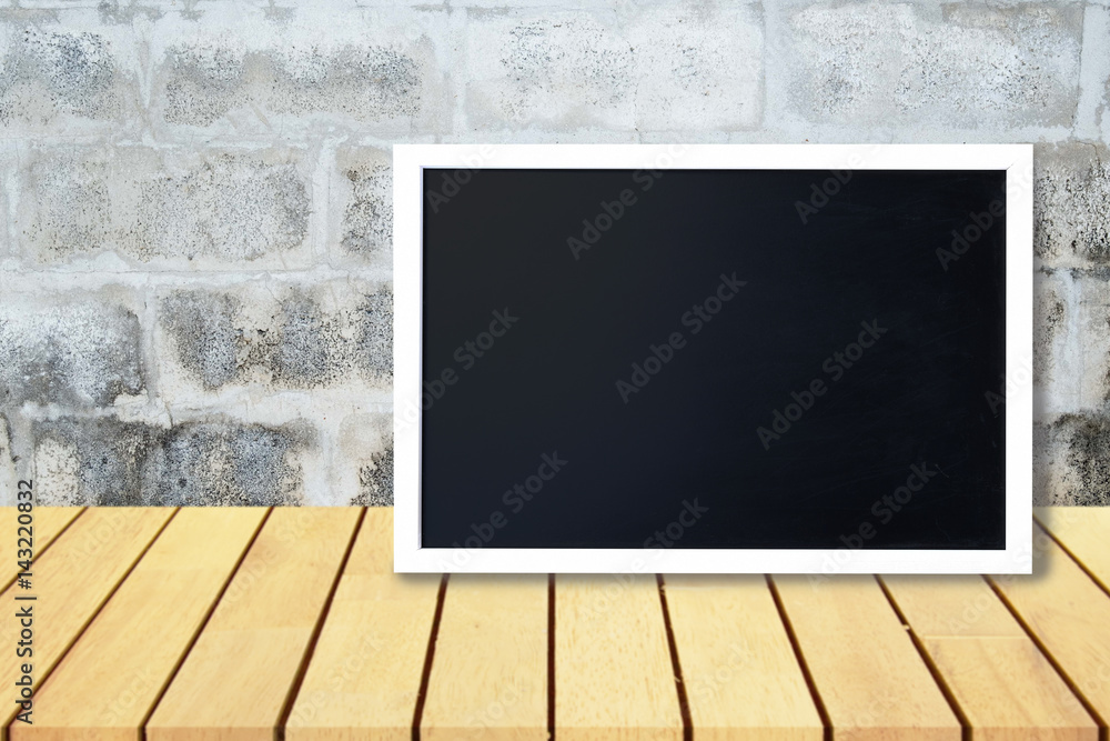Naklejka premium Blank black chalkboard lean on wooden table and old gray concrete wall, Blank copyspace for your text or design.
