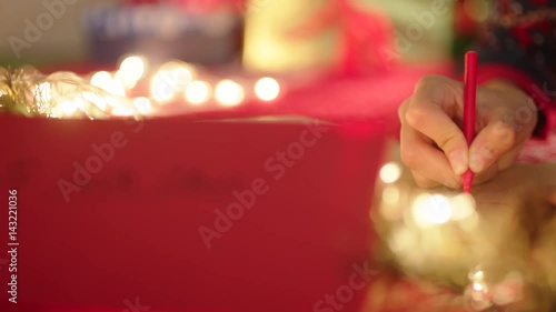 Red envelope with Santa Claus address. Hand is writing a letter on the background photo