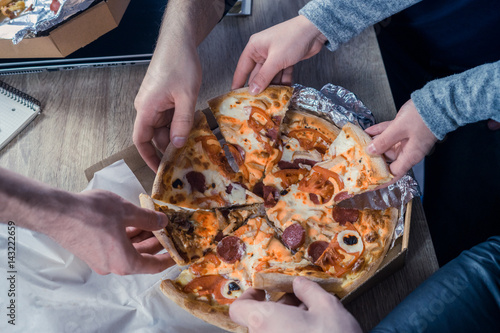 Eating pizza together in office. Top view of hands taking pizza. Concept of friendship at work unity teamwork partnership.