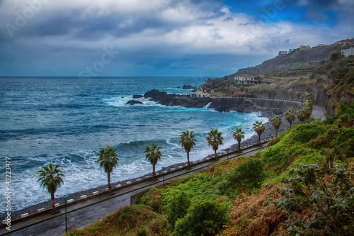 Old road along the ocean, waves, palm trees and mountains on Madeira Island, Portugal.