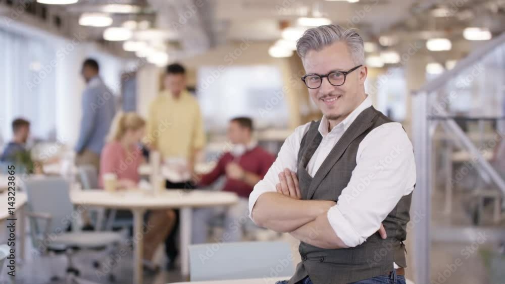 Portrait smiling business manager in office with staff working in background Portrait smiling business manager in office with staff working in background