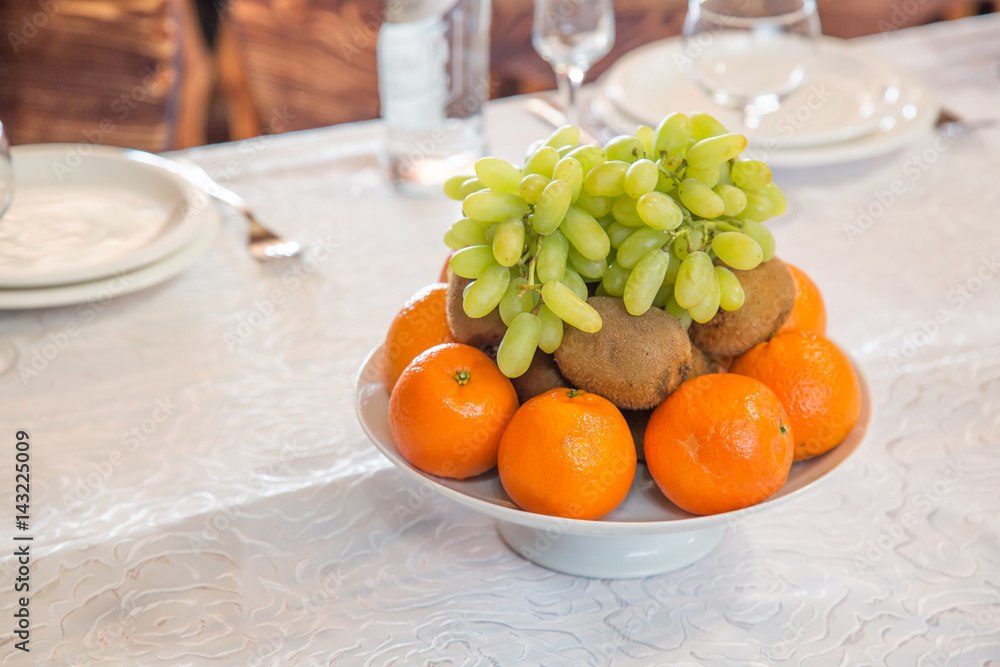 Plate with fruits oranges, grapes, kiwi with empty glasses and flatware on the background Plate with fruits oranges, grapes, kiwi with empty glasses and flatware on the background