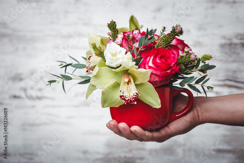 hand holding Small red vase with bouquet of flowers on gray space for text