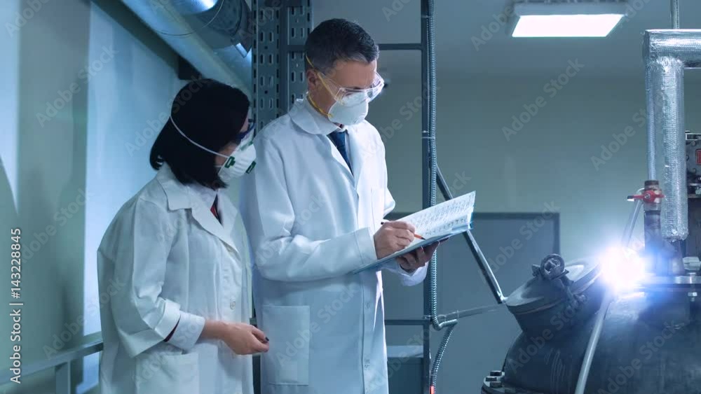 Man and woman with the notepad walking in a factory and inspecting. Horizontal indoors shot. Man and woman with the notepad walking in a factory and inspecting. Horizontal indoors shot.