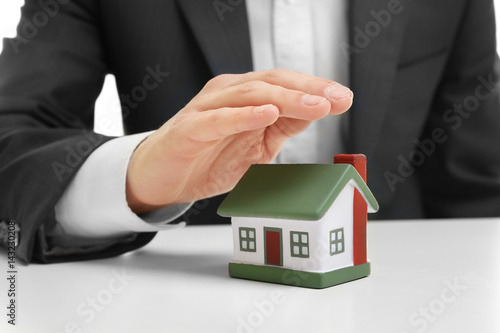 Insurance concept. Man covering with hand toy house on table