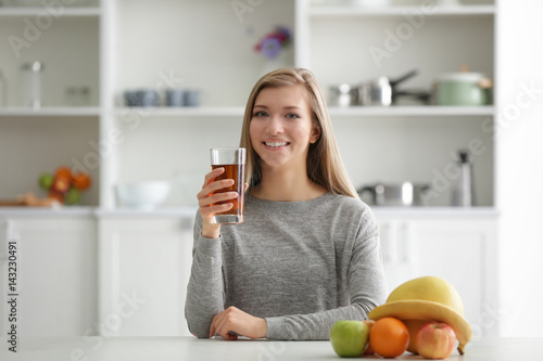 Young woman with glass of fresh juice at kitchen