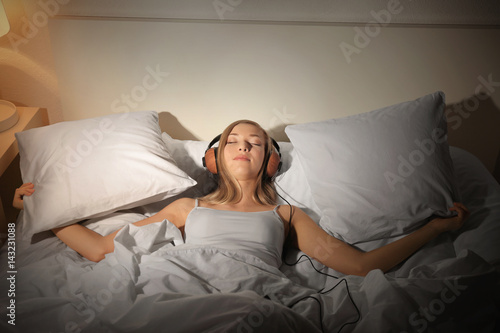 Beautiful young woman listening to music while resting in bed at home