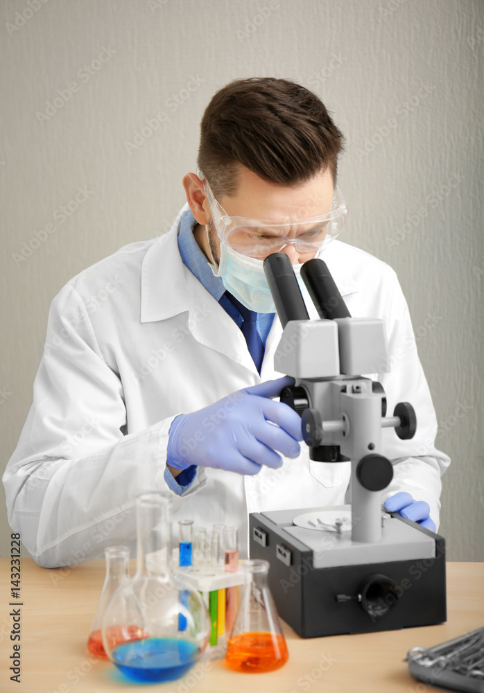 Young doctor working with microscope at table on light background