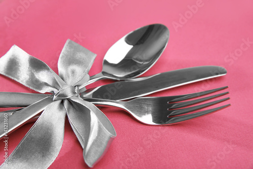 Cutlery set with ribbon bow on color background