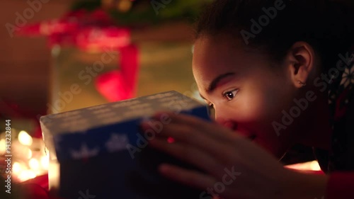 Young woman prying into the gift box on and putting her finger to lips asking do not tell to anybody photo