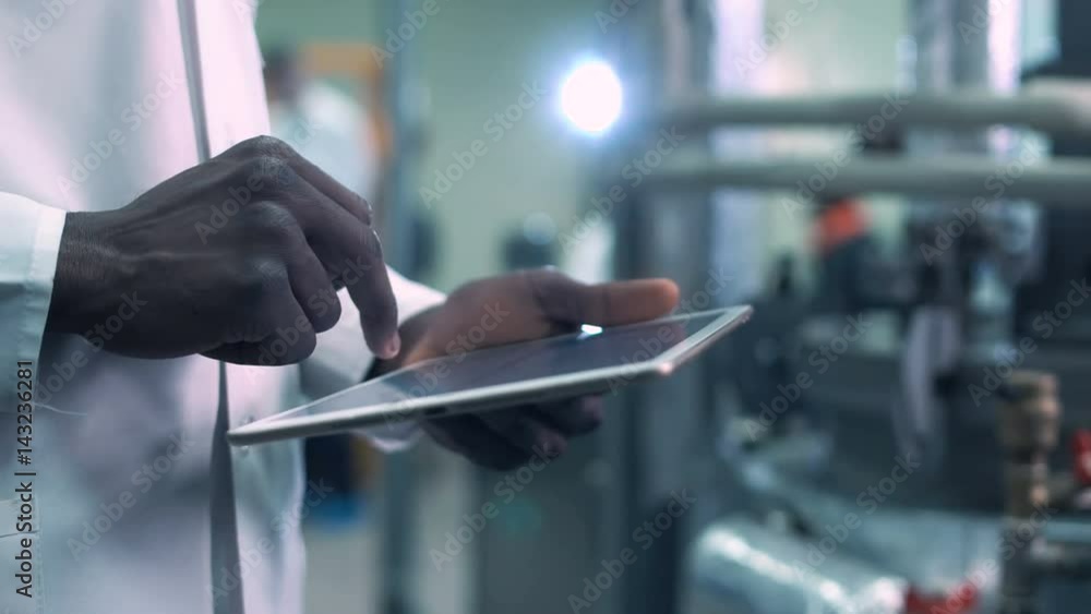 Close-up video of incognito Afro-American scientist hands in white lab coat holding a tablet and clicking on it while standing in laboratory Close-up video of incognito Afro-American scientist hands in white lab coat holding a tablet and clicking on it while standing in laboratory