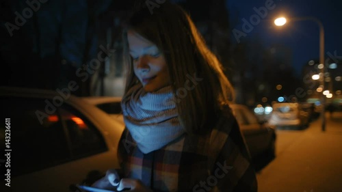 Young Woman is Walking in a Dark Street, Texting on her Phone and Smiling