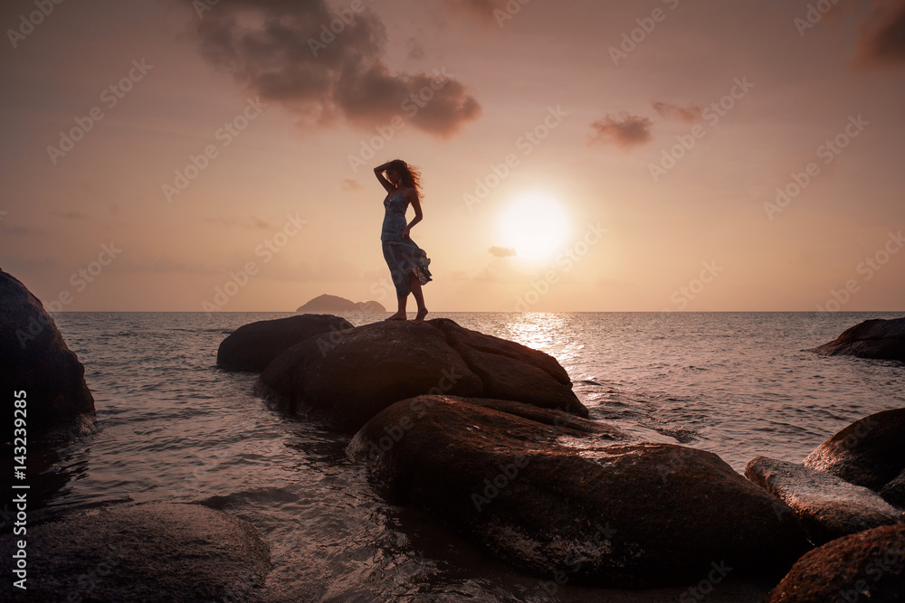 Fototapeta premium beautiful young woman silhoutte standing on stone at sunset