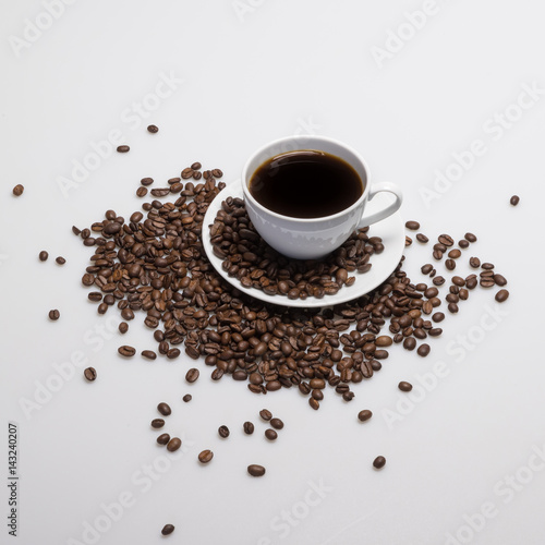 High angle view of a coffee cup and beans on a white and gray background.
