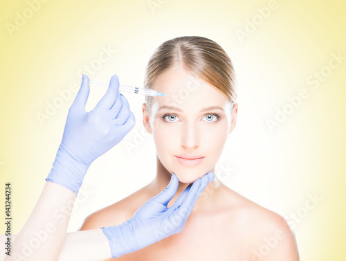 Young, beautiful and healthy woman having skin injections over yellow background. Plastic surgery concept.