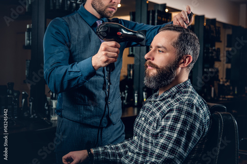 Hairdresser drying man's hair with hairdryer in a saloon.