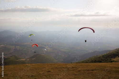 Some colorful paragliders flying over a mountain scenery, with some faint sunrays.
