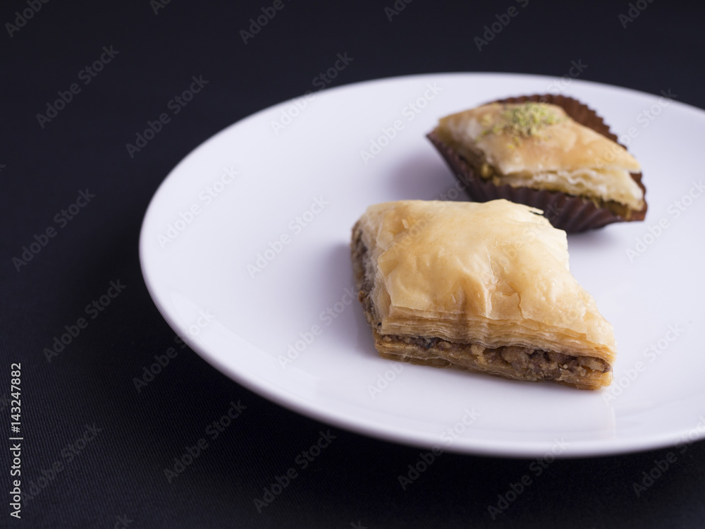 Baklava with nuts and pistachio nuts placed on white plate, isolated on black background Baklava with nuts and pistachio nuts placed on white plate, isolated on black background