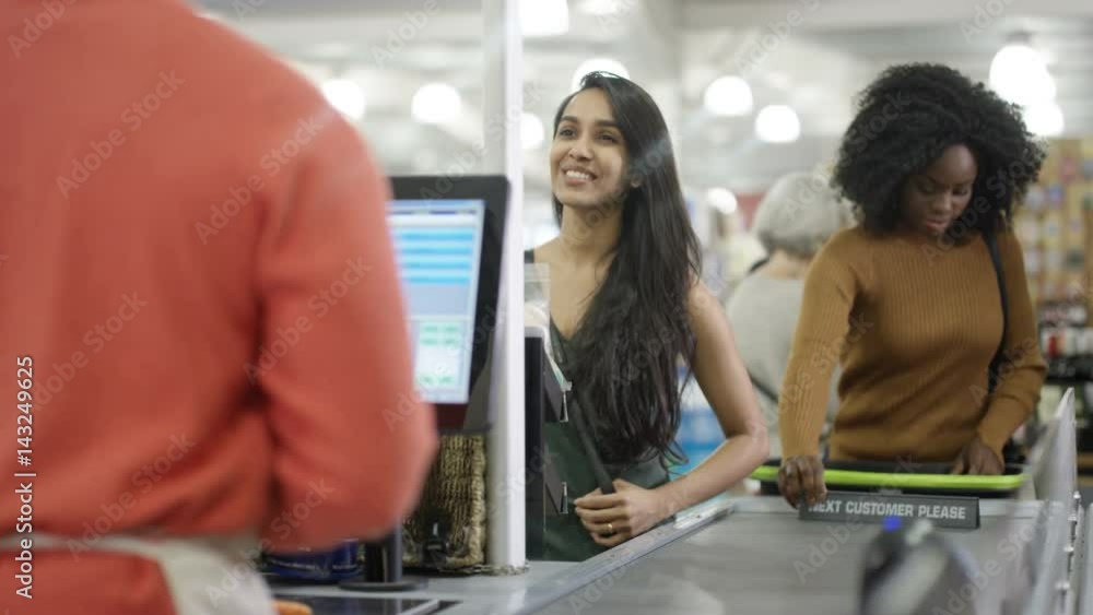 Friendly cashier taking payment from a customer at grocery store checkout Friendly cashier taking payment from a customer at grocery store checkout