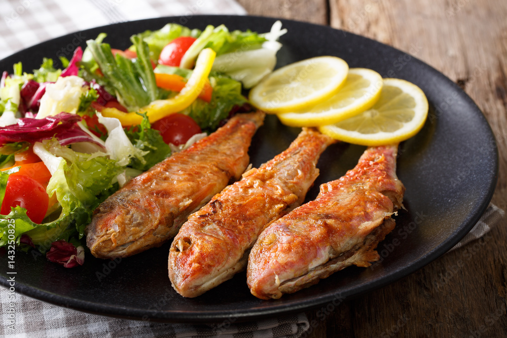 Delicious fish red mullet with fresh mix vegetable salad close-up. Horizontal Delicious fish red mullet with fresh mix vegetable salad close-up. Horizontal