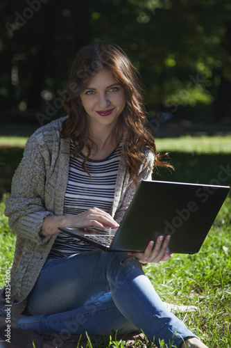 beautiful happy woman working working with a laptop in a green park outdoors (freelance, time management, success, freedom)