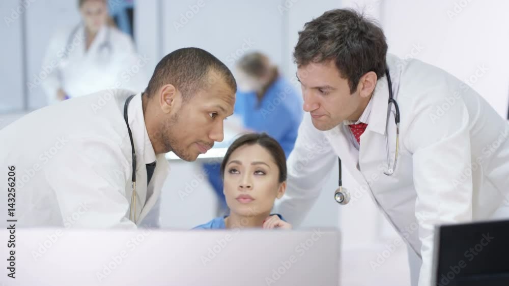 Medical team in modern hospital looking at computer & having a meeting Medical team in modern hospital looking at computer & having a meeting
