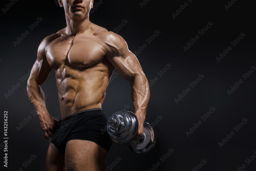Strong bodybuilder with perfect abs, shoulders, biceps, triceps and chest. Handsome power athletic man with dumbbell.