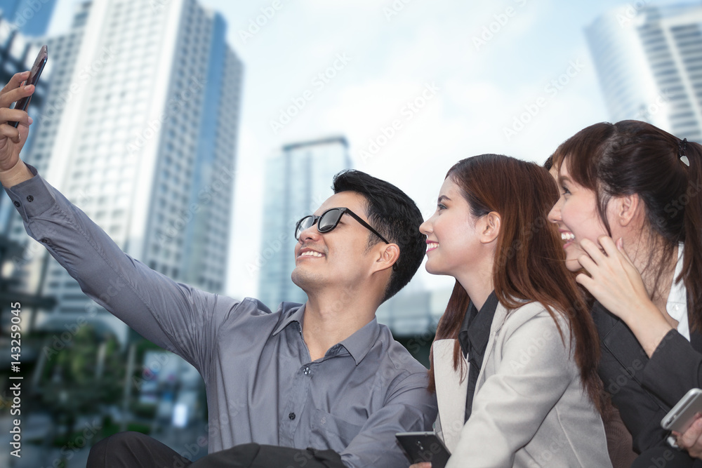 businessman sitting and using phone to take photo as selfie with colleague together and modern office building background