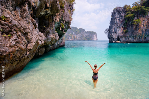 Vacation and freedom. Happy young woman rising hands up standing on tropical beach enjoying beautiful view in Thailand.