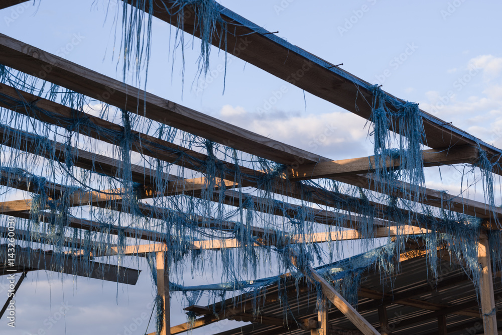 Fototapeta premium Wooden frame with thin pieces of torn blue fabric on an abandoned market on the background of sky with clouds, Ukraine.