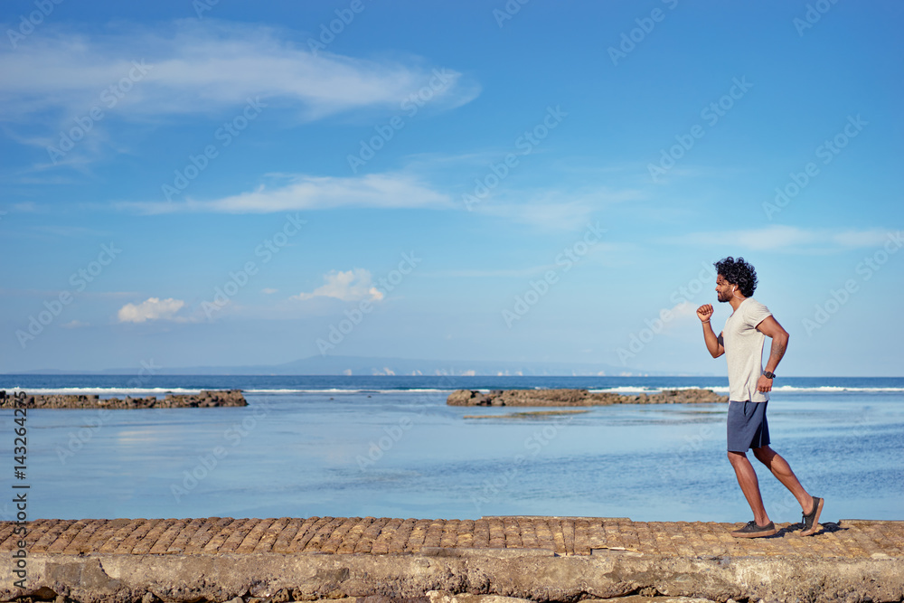 Sports lifestyle. Happy young african man jogging on the sea shore.