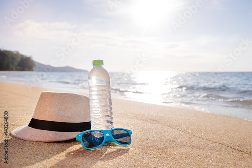 Vacation and protection. Essentials on the sea beach. Bottle of drinking water, sunglasses and hat.