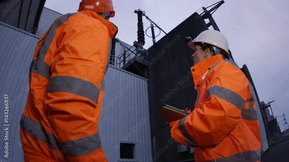 Male & female engineers at power station, looking at computer tablet Male & female engineers at power station, looking at computer tablet