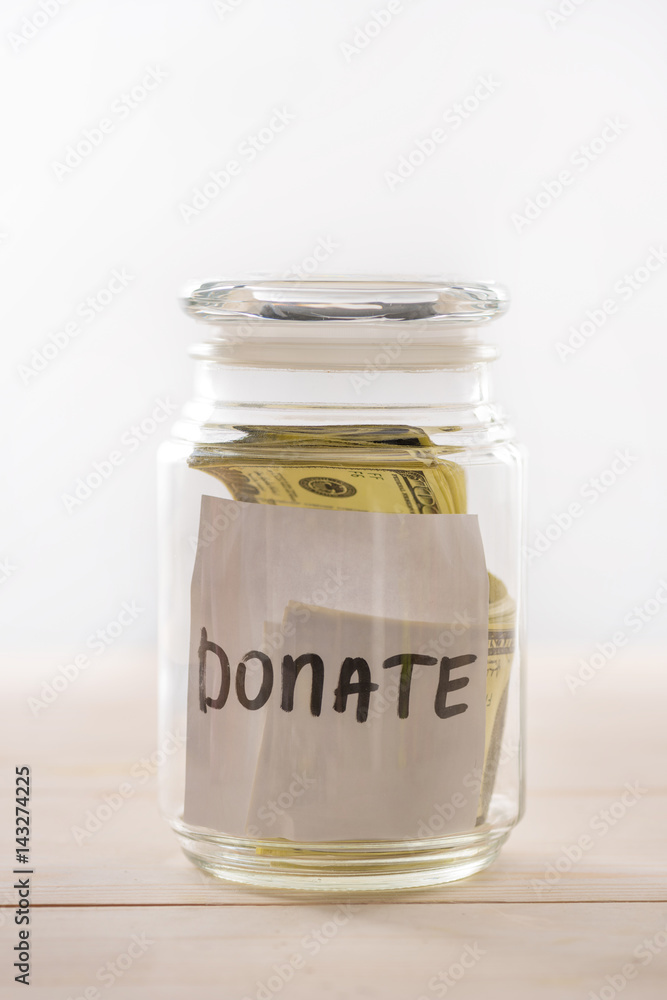 Close-up view of dollar banknotes in glass jar with donate lettering, donation concept Close-up view of dollar banknotes in glass jar with donate lettering, donation concept